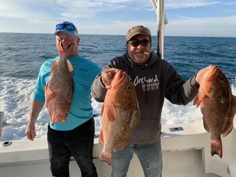 Two anglers offshore holding up three red grouper