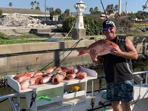 An angler at the dock holding a red snapper over a table of the day’s catch
