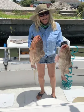 An angler at the dock holding up two grouper
