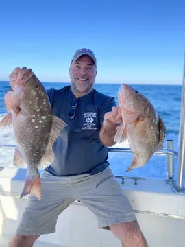 An angler offshore holding a grouper in each hand