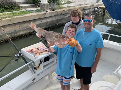 Two young anglers and an adult on deck with a large grouper