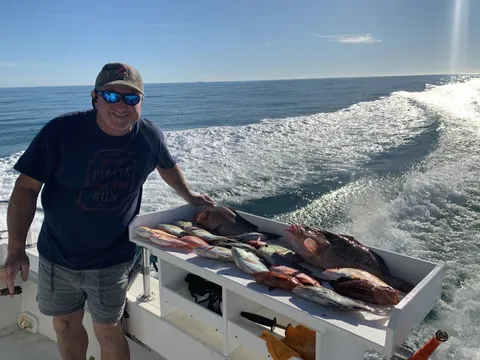 An angler beside a box of red fish on the back deck, the wake behind the boat