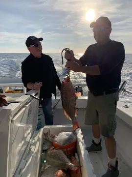 Two anglers on deck, one holding up a fish, with a cooler of the catch