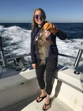 An angler on deck holding up a grouper, the wake behind the boat