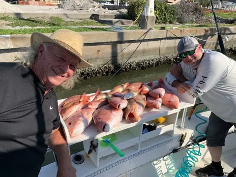 Two anglers at the dock with a table piled with red snapper