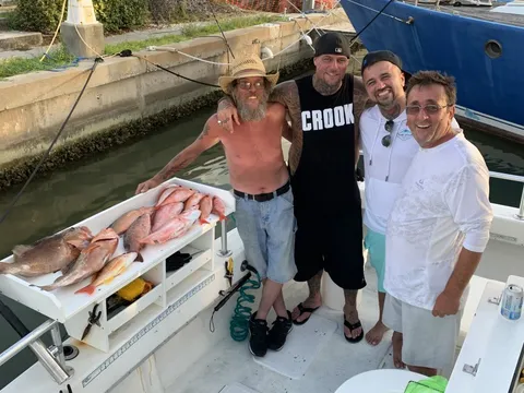 Four anglers at the dock behind a cleaning table of red snapper